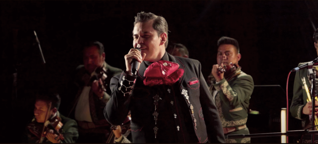 Raúl Sandoval canta apasionadamente en el escenario, vestido de charro, acompañado por el mariachi Los Gavilanes de José Alfredo Jiménez, mientras interpreta “Deja Que Salga La Luna” bajo una luz tenue y cálida que evoca la atmósfera de la música ranchera tradicional.