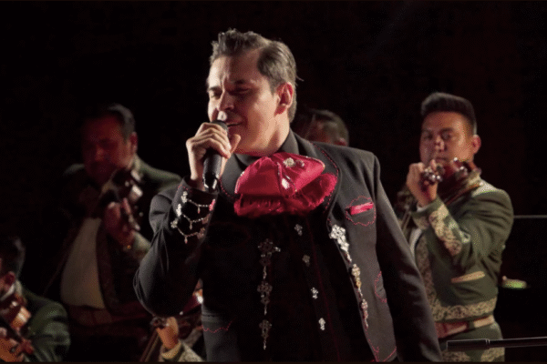 Raúl Sandoval canta apasionadamente en el escenario, vestido de charro, acompañado por el mariachi Los Gavilanes de José Alfredo Jiménez, mientras interpreta “Deja Que Salga La Luna” bajo una luz tenue y cálida que evoca la atmósfera de la música ranchera tradicional.