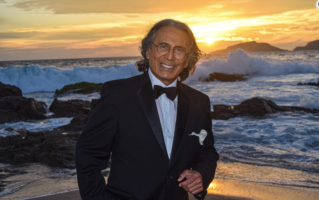 King Clave posando frente a la playa con el mar de fondo, mostrando una expresión relajada y elegante.